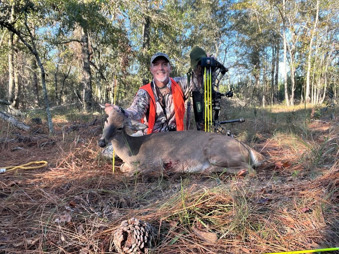 Hunter in blaze orange with a recovered doe, yellow arrows in the foreground