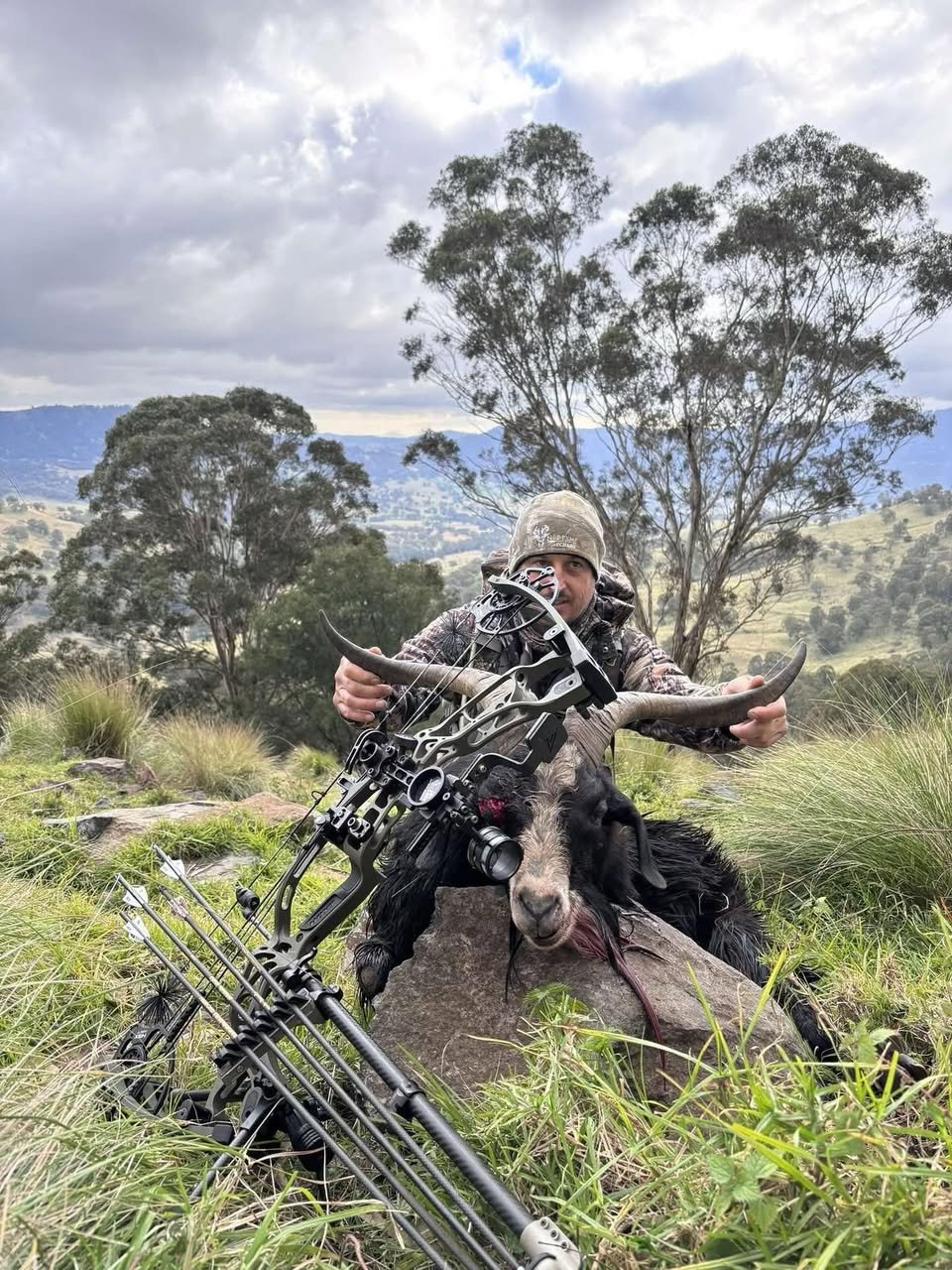 Hunter crouched on the rocks with a black goat and crossbow