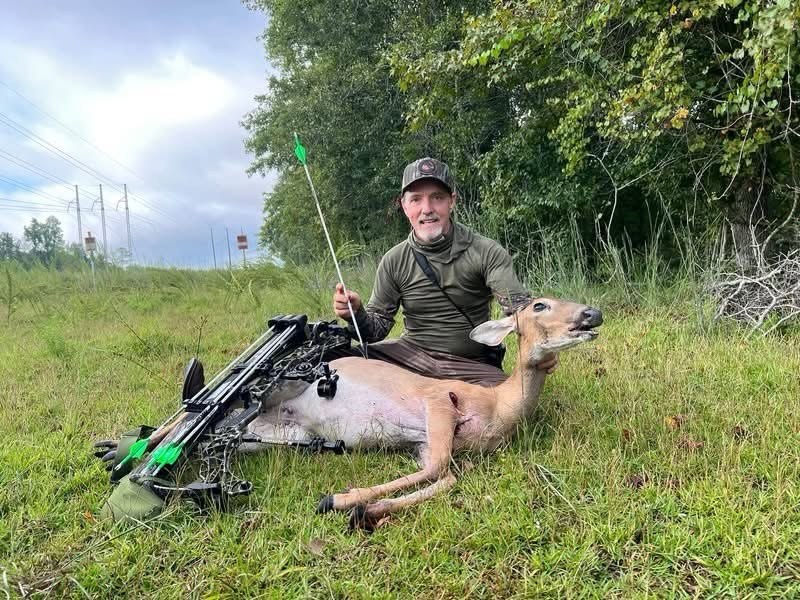 Hunter with a whitetail doe, holding a white carbon arrow with green fletching
